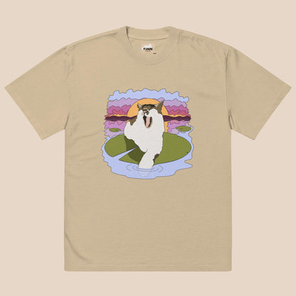 Beige t-shirt with a graphic of a cat on a lily pad against a sunset background